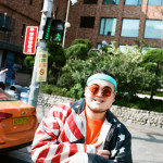 성조기 패턴 가죽 재킷 빈티지산타, 치노 팬츠 디키즈, 겹쳐 쓴 틴트 선글라스 모두 프로젝트 프로덕트, 오렌지 컬러 티셔츠 본인 소장품, 헤어밴드와 목걸이, 미니 백팩 스타일리스트 소장품.